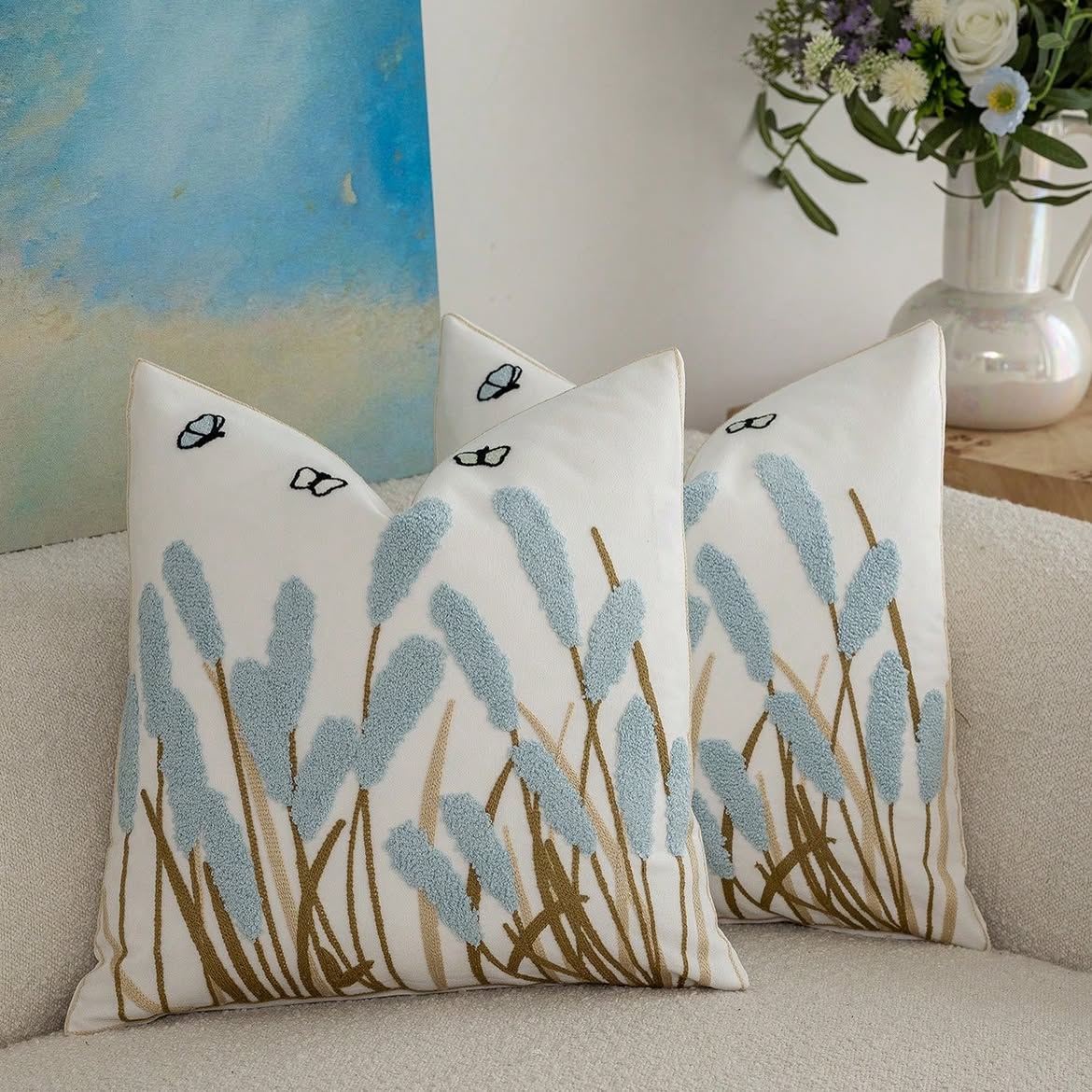 Ivory cushion cover with powder blue textured meadow reeds, embroidered stems, butterflies, and coordinating piping.