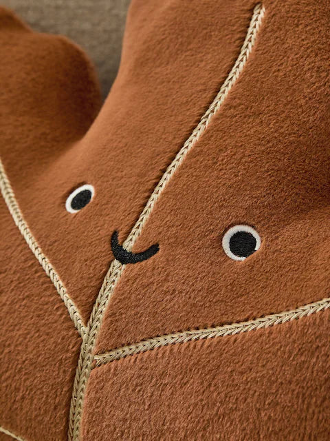 Close up of embroidered smiley face detail on caramel velvet maple leaf cushion