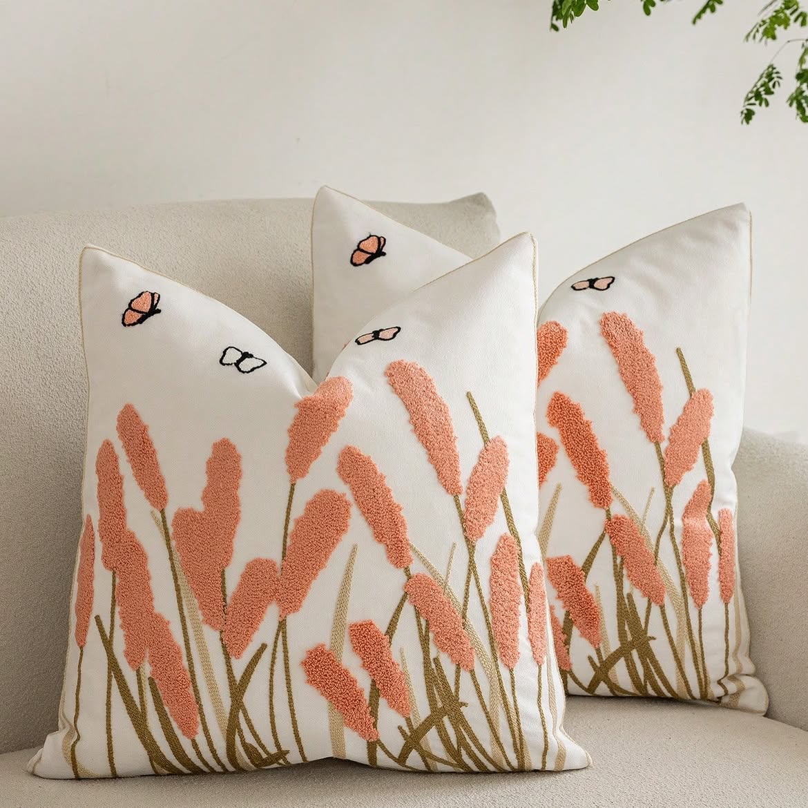 Ivory cushion cover with blush pink textured meadow reeds, embroidered stems, butterflies, and coordinating piping.