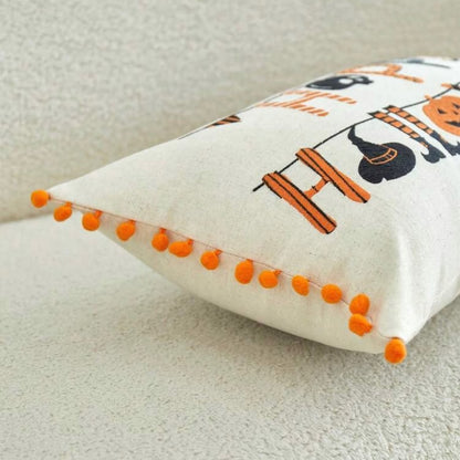 Side view of Happy Halloween embroidered lumbar cushion cover showing orange pom-pom trim detail along edge on cream surface