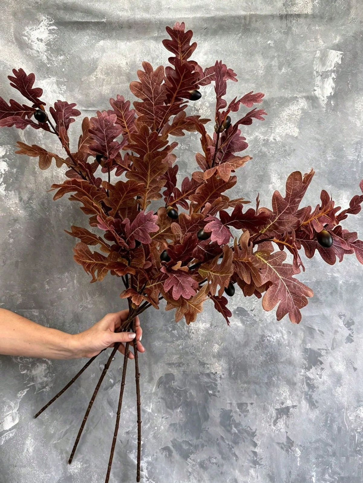 Bundle of faux burgundy oak leaf branches with acorns held in hand