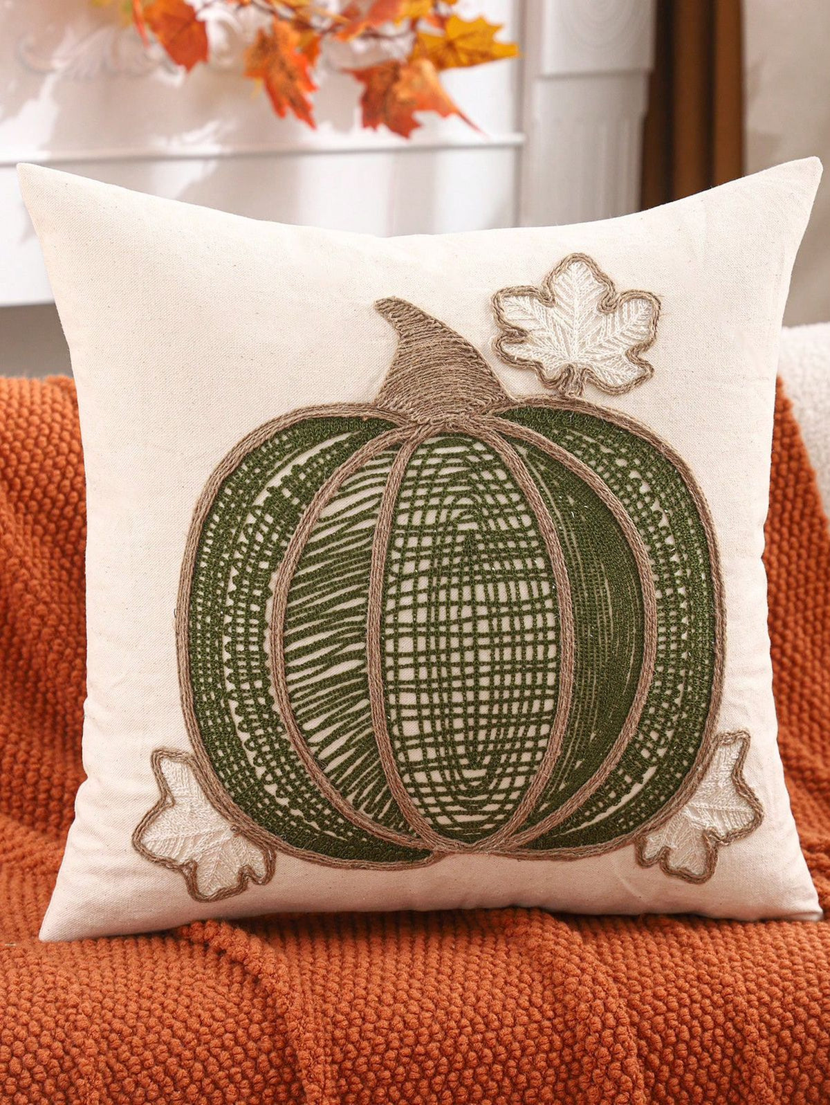 Lace embroidered pumpkin pillow cover in olive green with jute rope ribs and maple leaf accents on rust sofa