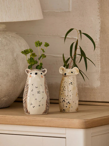 Hedgehog and mouse ceramic bud vases with green stems on oak sideboard in warm neutral living room