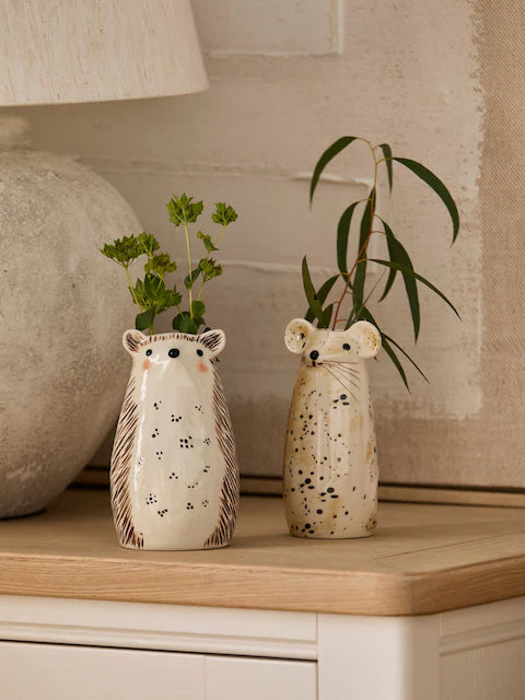 Hedgehog and mouse ceramic bud vases with green stems on oak sideboard in warm neutral living room