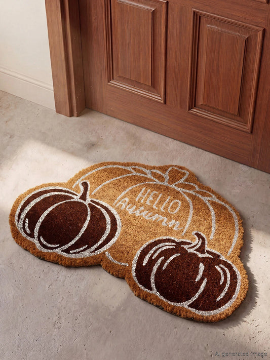Hello Autumn pumpkin shaped coir doormat styled in front of wooden door on grey concrete floor - lifestyle shot