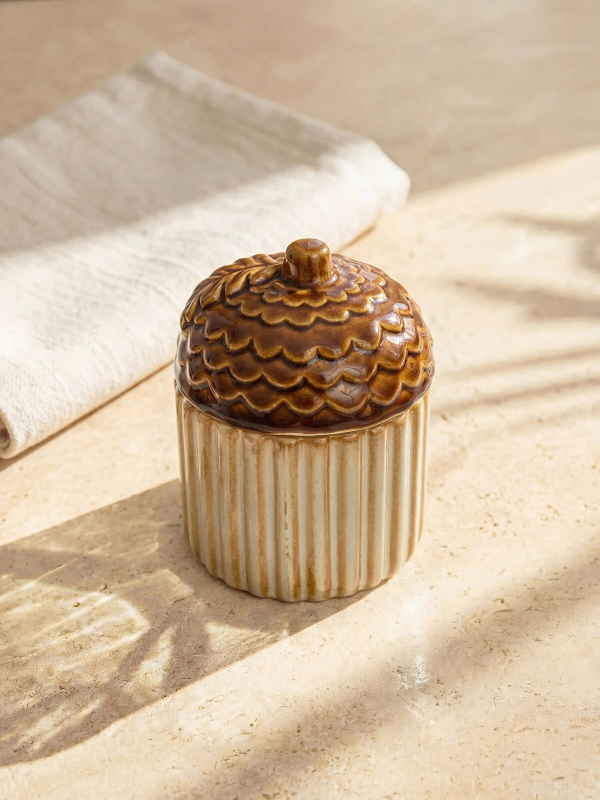 Ceramic acorn sugar bowl with lid on sandy linen surface in warm golden autumn light lifestyle shot