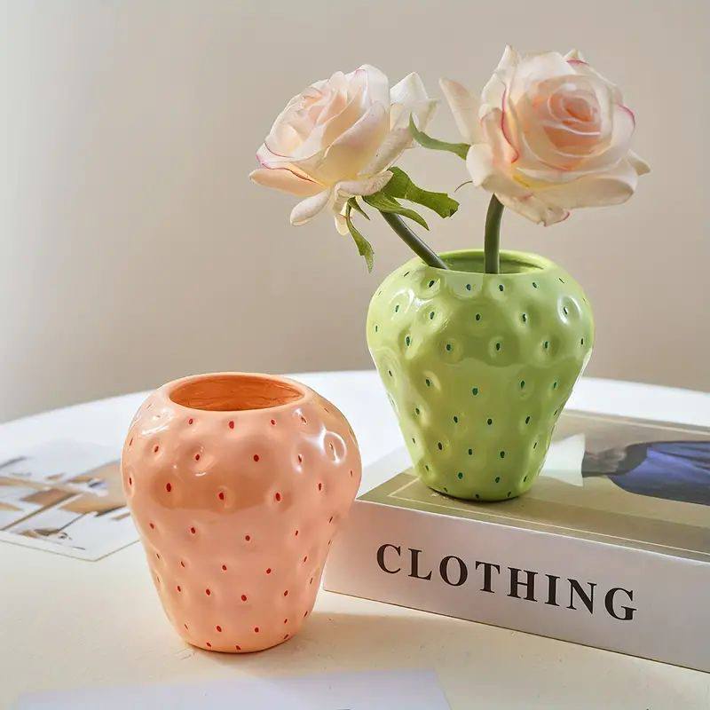 Two ceramic vases, one pink and one green, with flowers on a surface.